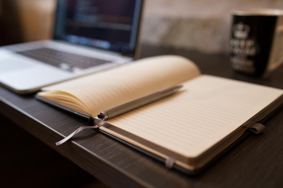 Quaderno a righe e penna appoggiati su una scrivania accanto a una tazza