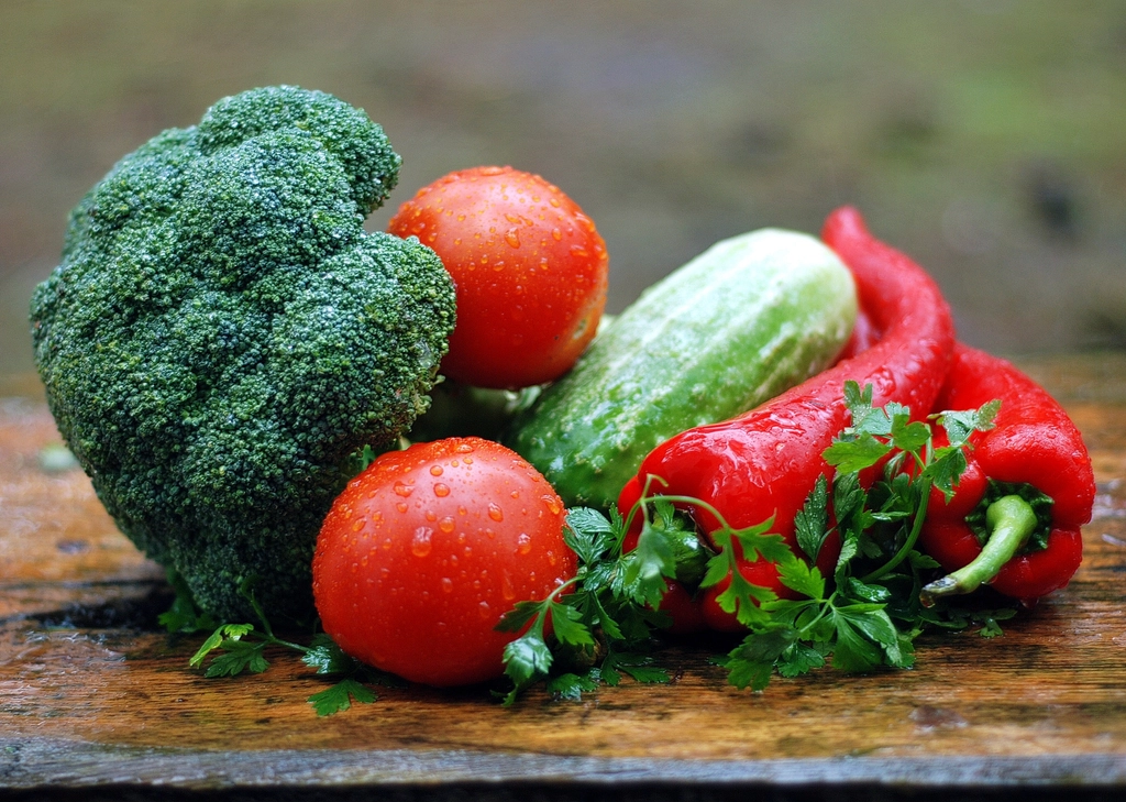 Verdure fresche disposte su un tavolo di legno accanto a un tagliere vuoto