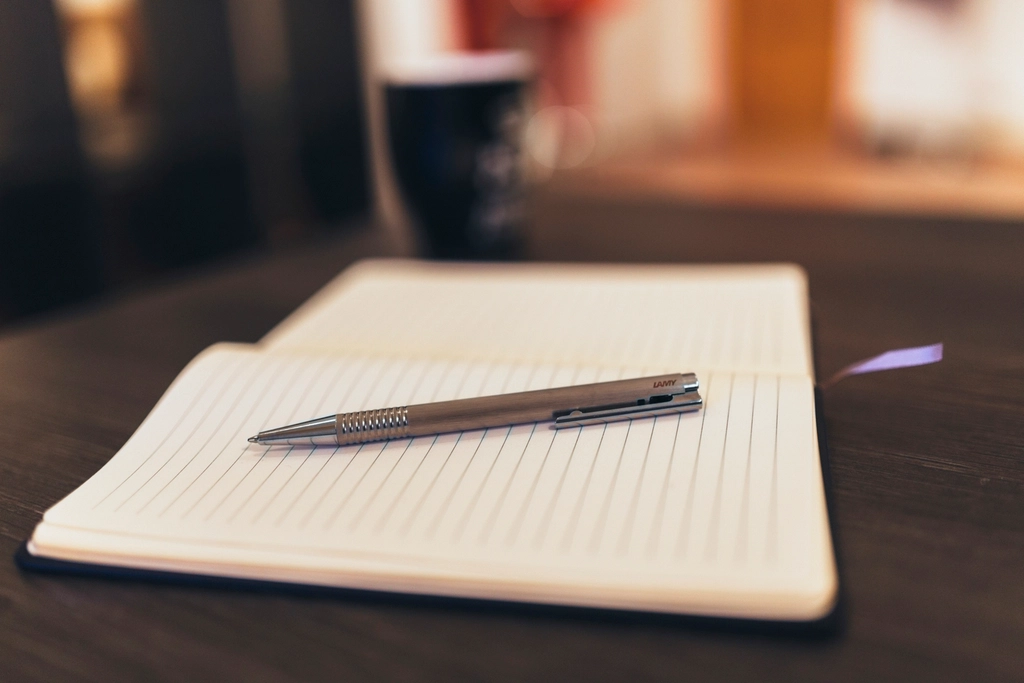 Quaderno aperto con una penna appoggiata sulla pagina accanto a una tazza